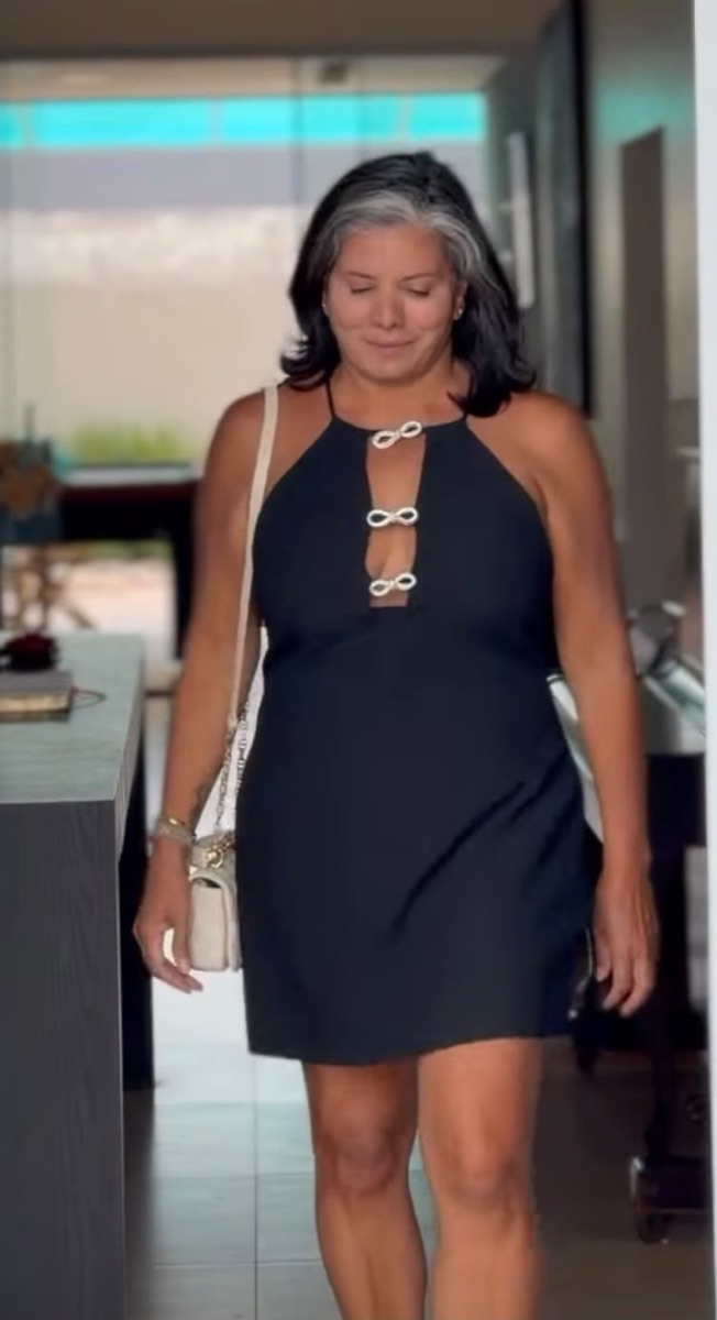 Doró com vestido preto de alças e laços prateados no decote, bolsa clara de corrente