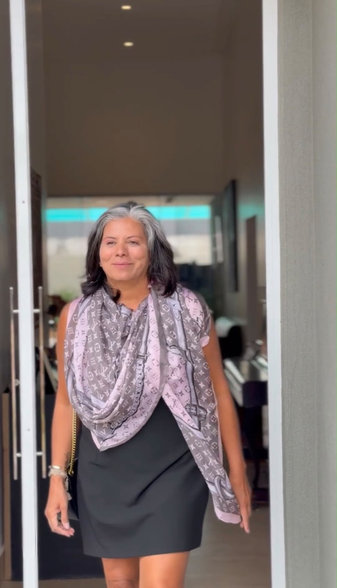 Doró com o mesmo vestido preto e um lenço estampado rosa e cinza enrolado no pescoço e caindo sobre o corpo